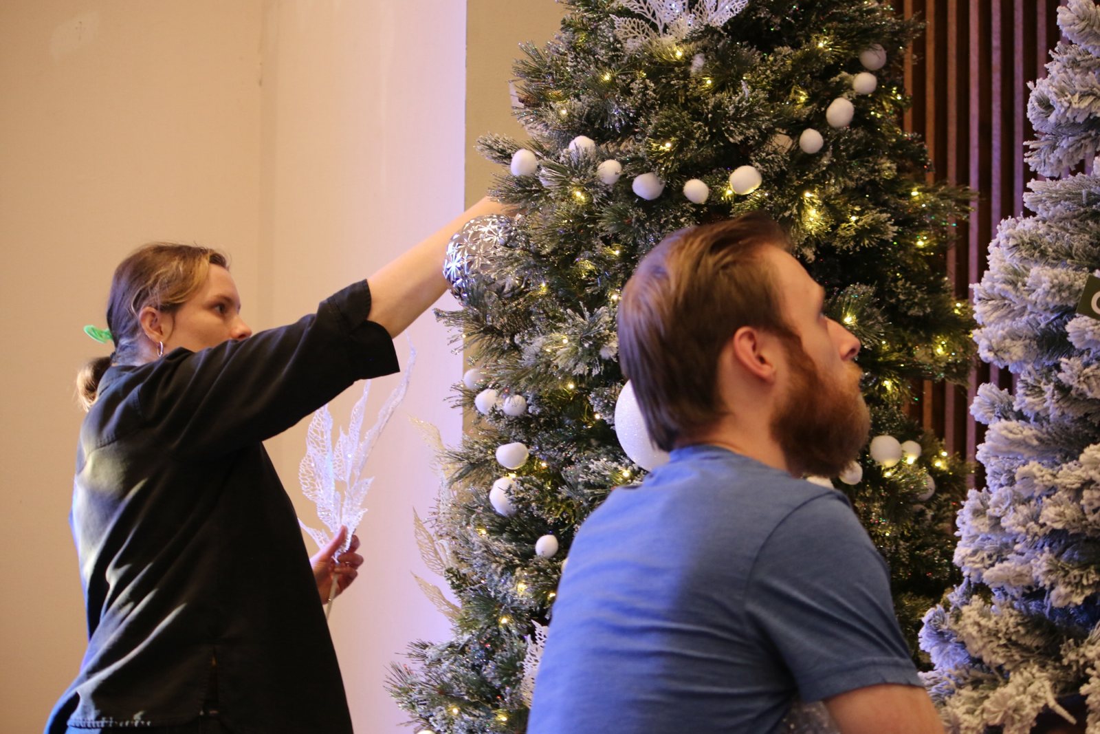 A volunteer hangs an ornament on a snow-flocked Christmas tree in the church
