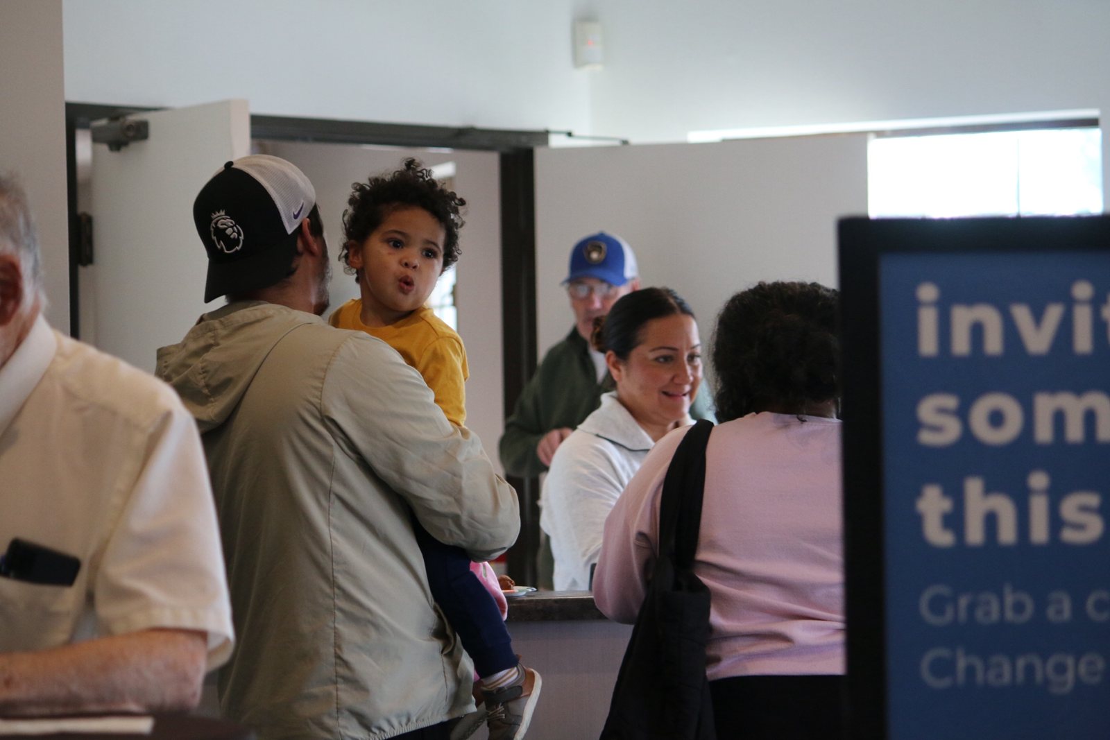 A dad holds his toddler while families chat in the church lobby