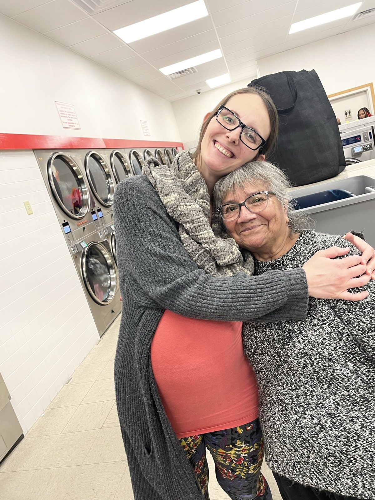 Two women share a hug at a Laundry Love night in the laundromat