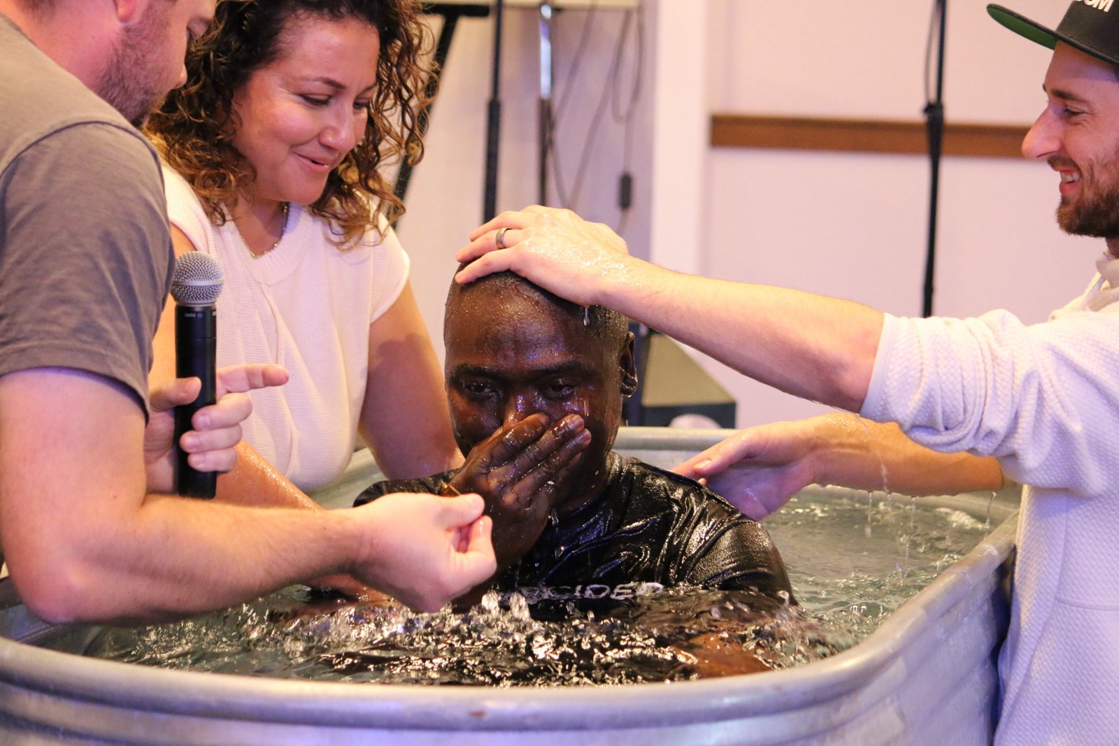 A man overcome with joy in the baptism tank as friends lay hands on him